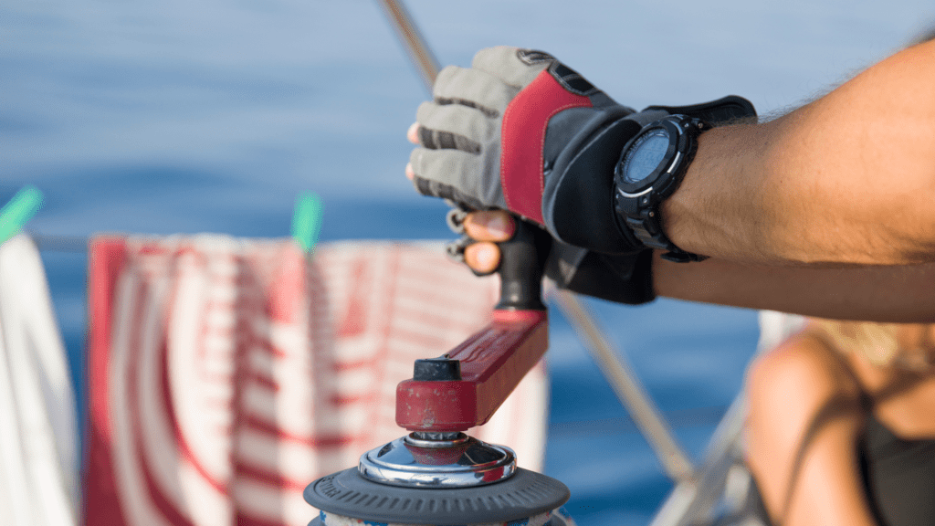 Up close of grey and red sailing gloves on hands winding a crank