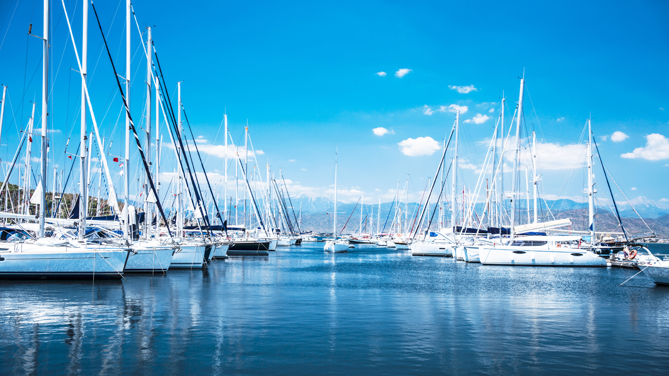 Centre view of a marina with a row of white yachts harboured at both sides on blue water