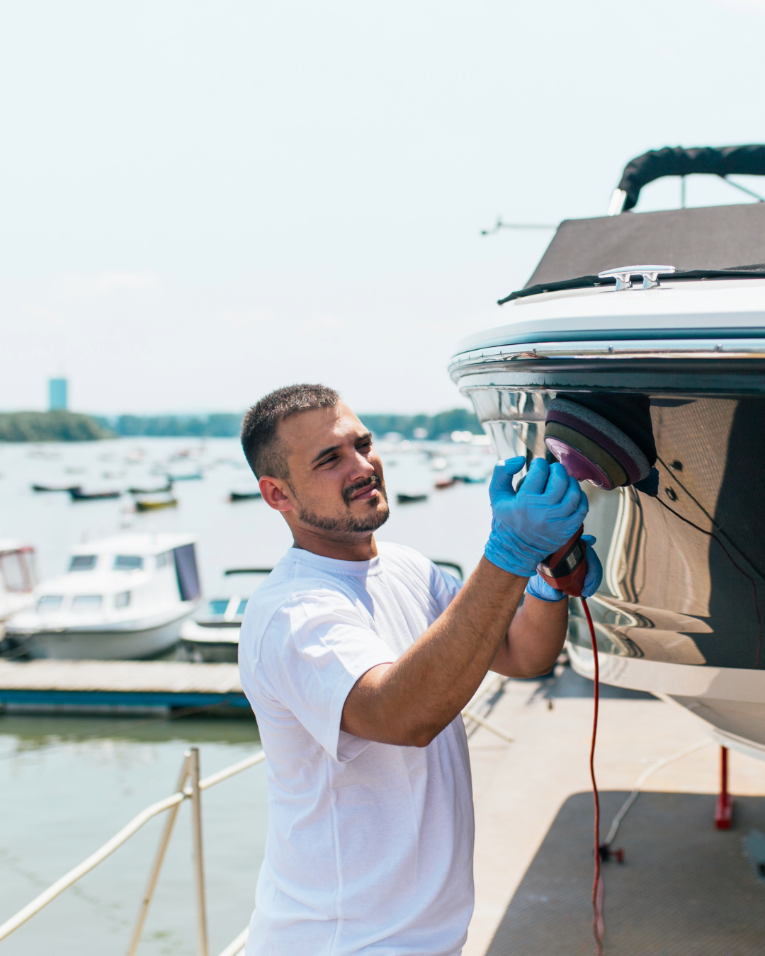 http://Man%20with%20orbital%20polisher%20polishing%20boat%20in%20marina.%20Selective%20focus.